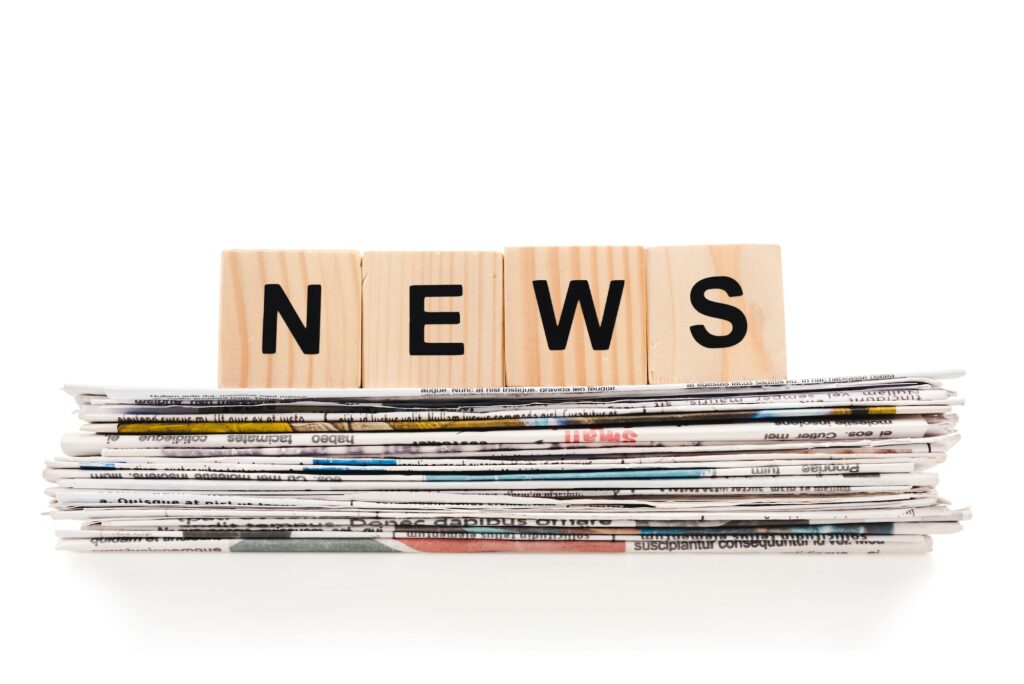 wooden blocks with news lettering on pile of print newspapers isolated on white